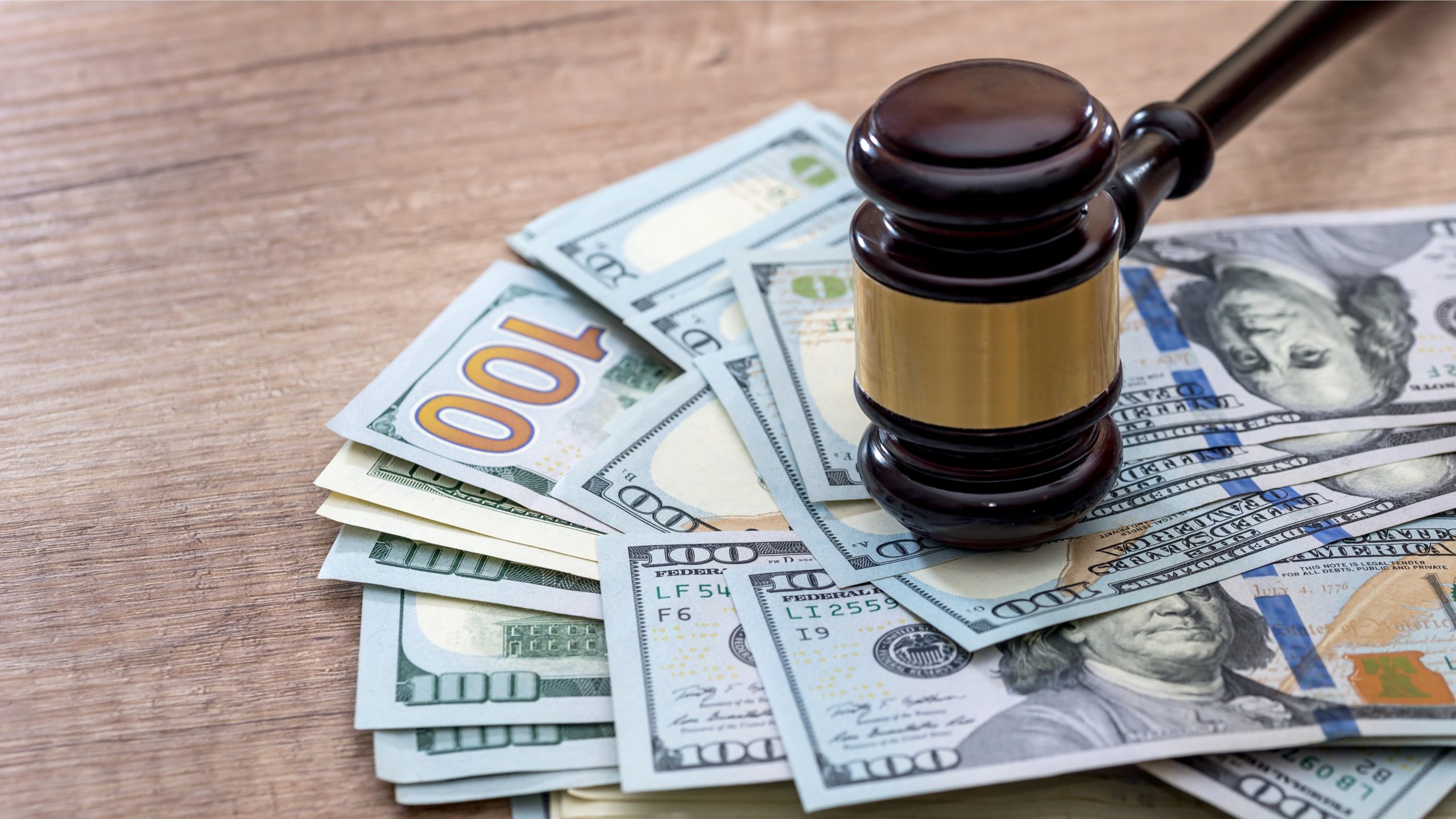 a judges gavel rests on a pile of US dollars on a wooden table